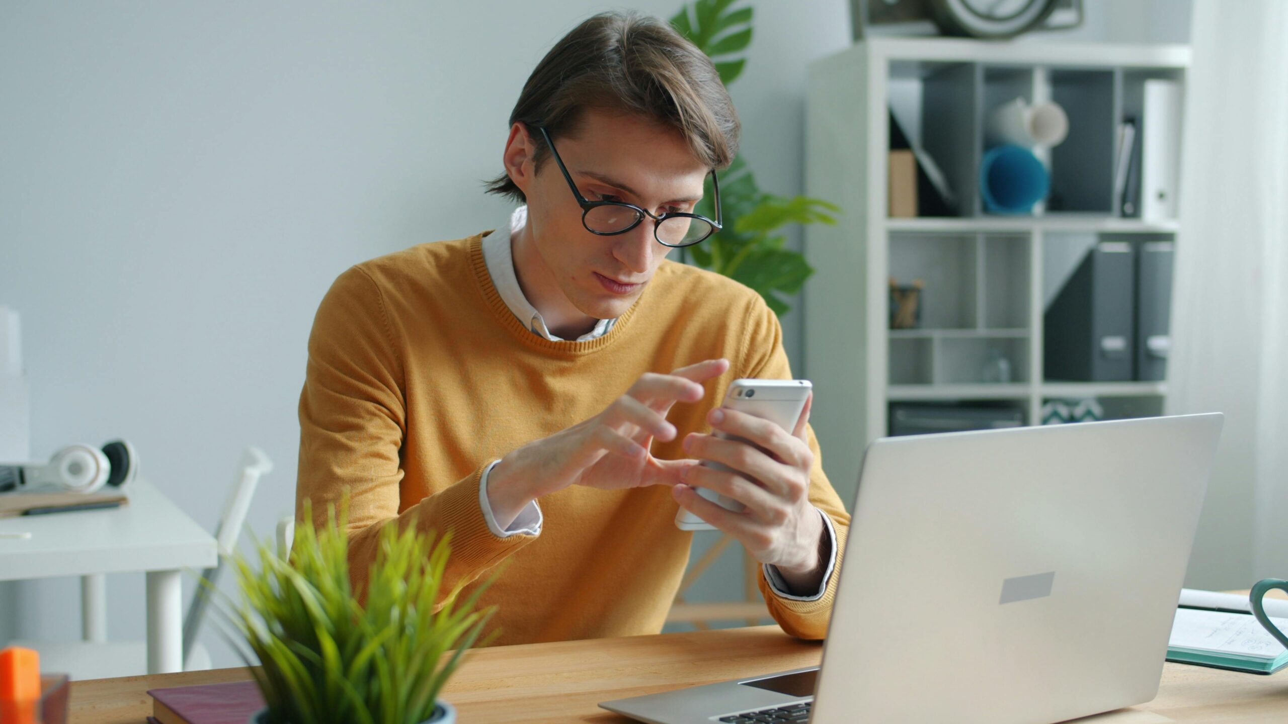 Empleado en teletrabajo consultando el movil junto al portatil para registrar su jornada
